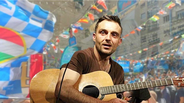 Cristian Vollaro che suona la chitarra davanti a una folla in festa con bandiere del Napoli